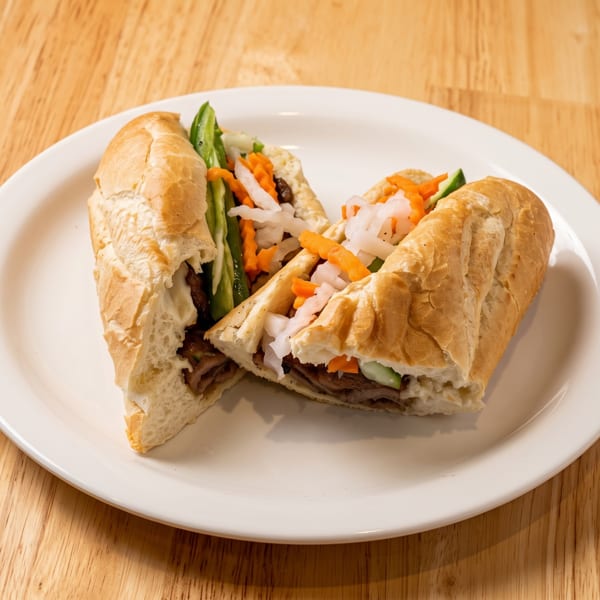 Banh mi sandwich cut in half on a white plate, revealing meat, pickled carrots, and daikon.