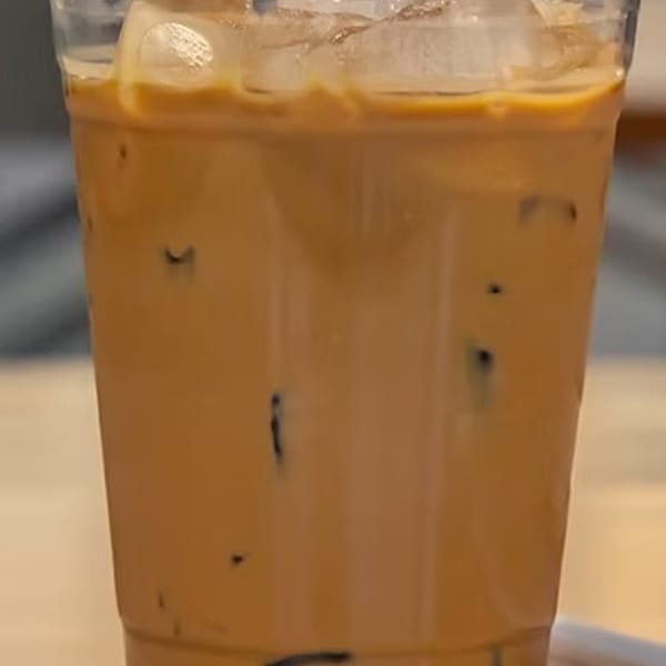 Clear plastic cup filled with iced coffee and ice cubes on a light surface.