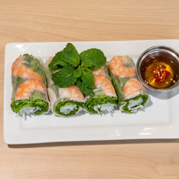 Four shrimp spring rolls with mint garnish and chili dipping sauce on a white plate.