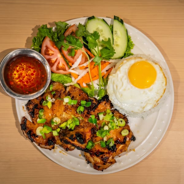 Grilled chicken with rice, fried egg, fresh salad, and chili dipping sauce.
